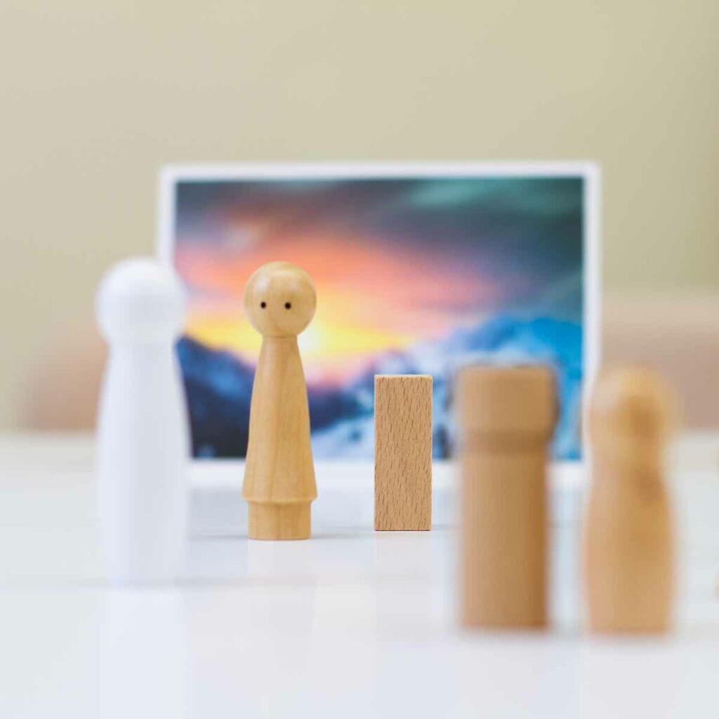 Foto einer mit Holzfiguren und Bildkarten nachgestellte Coaching-Szene: Die Hauptfigur steht vor einer Bildkarte mit Sonnenaufgangsszenerie und blickt auf eine gegenüberstehende Holzfigur. Versetzt stehen drei weitere Figuren.